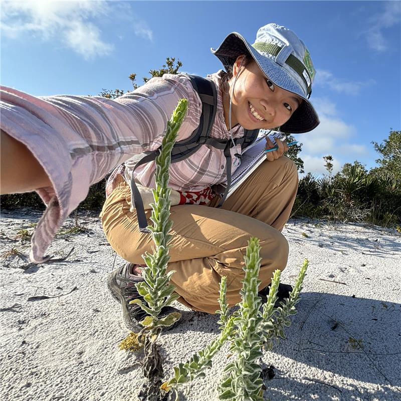 young woman kneeling near a plant and smiling